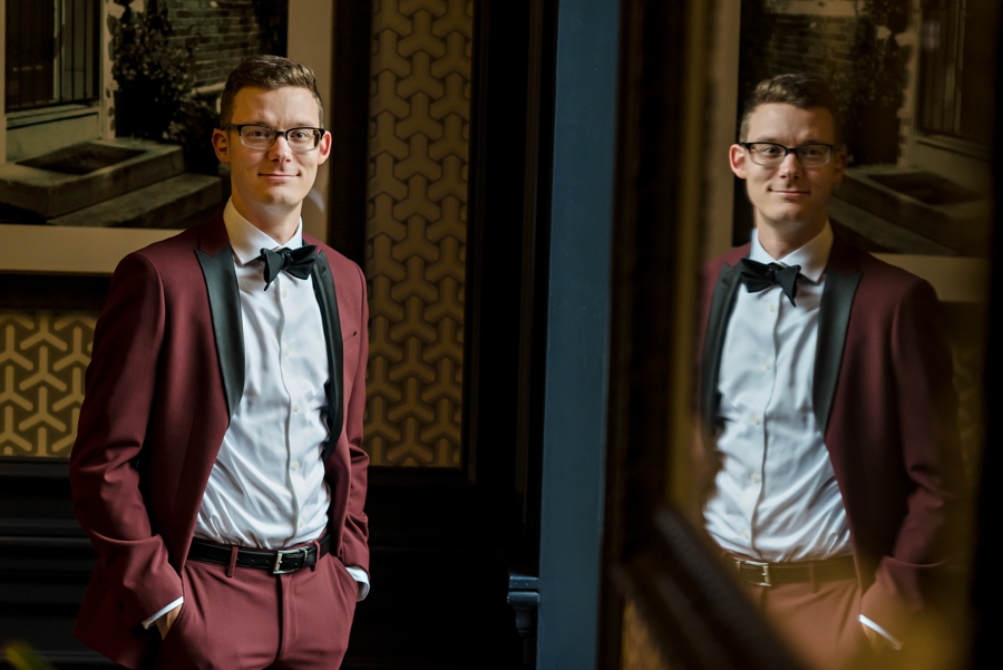A portrait of a groom in a maroon suit.